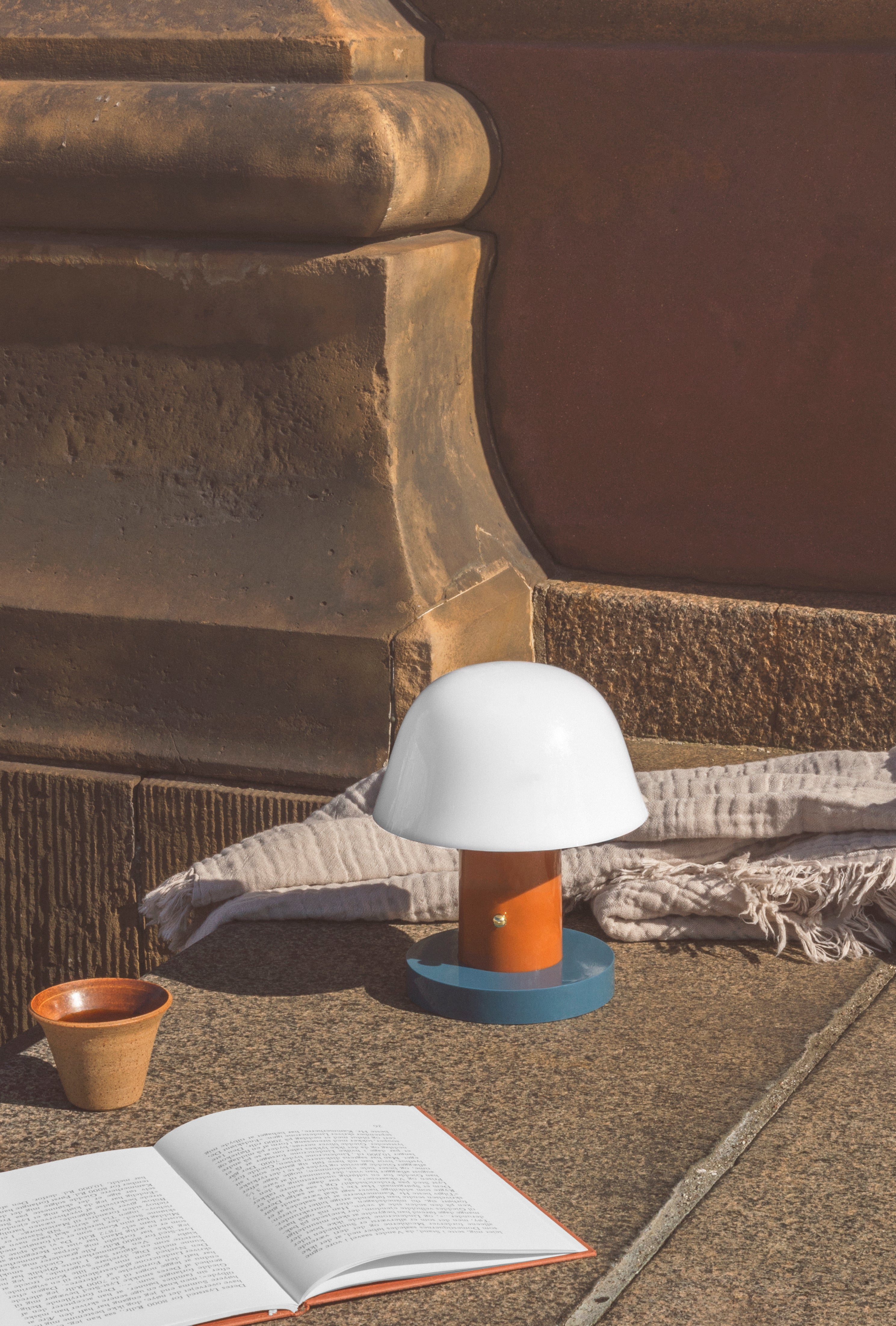 Draagbare lamp SETAGO JH27 met een crèmekleurige kap en een oranje-blauwe voet.