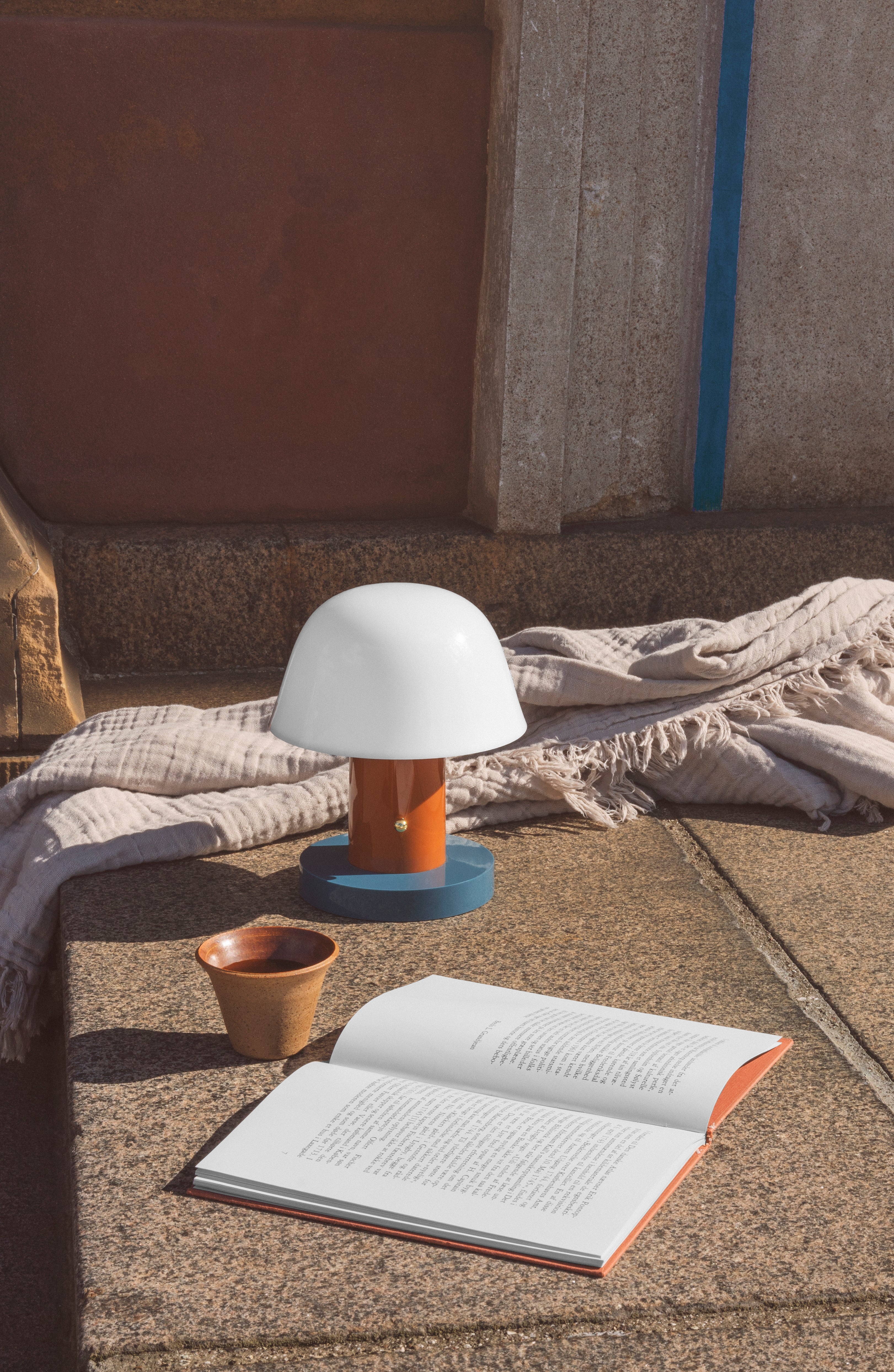 Draagbare lamp SETAGO JH27 met een crèmekleurige kap en een oranje-blauwe voet.