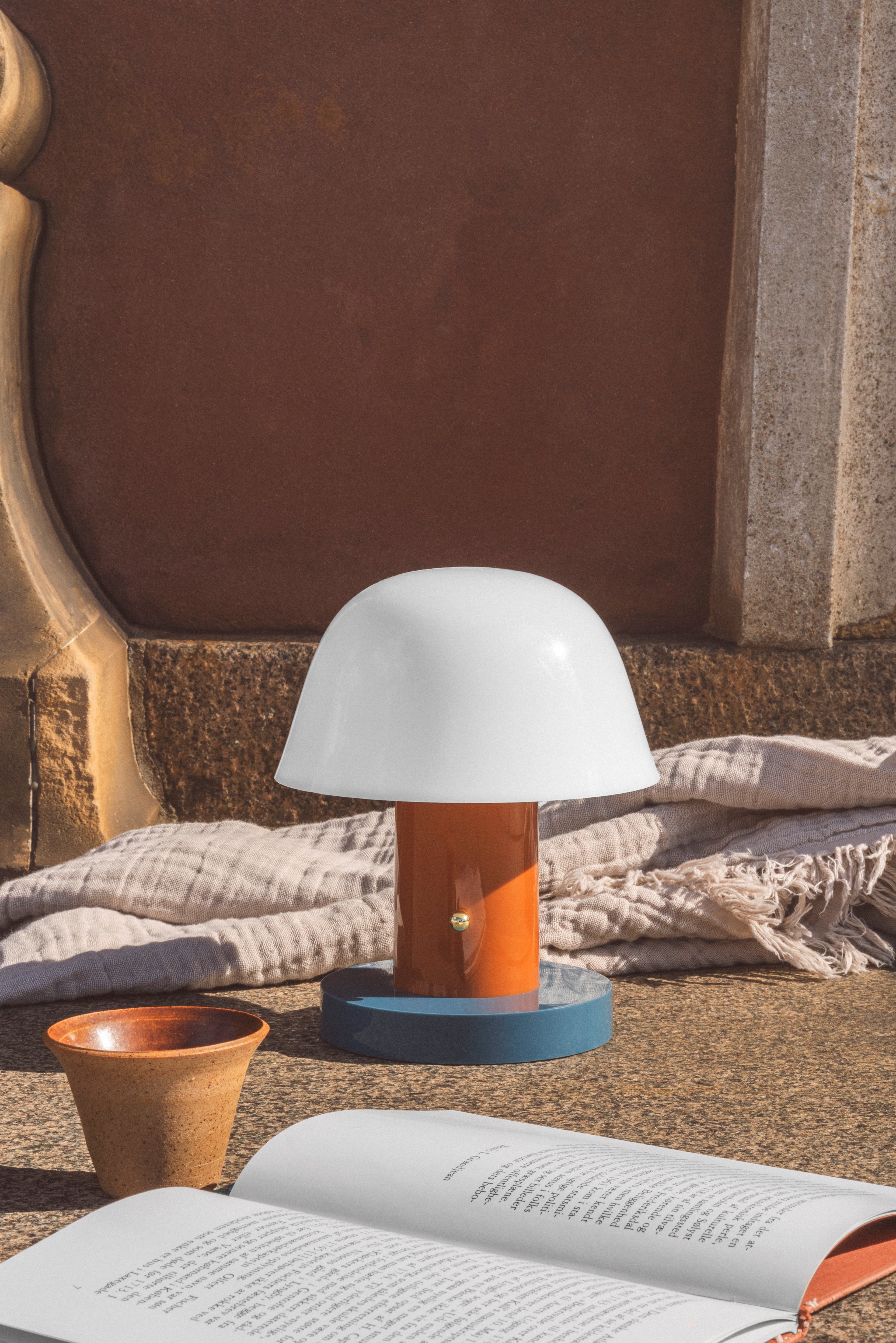Draagbare lamp SETAGO JH27 met een crèmekleurige kap en een oranje-blauwe voet.